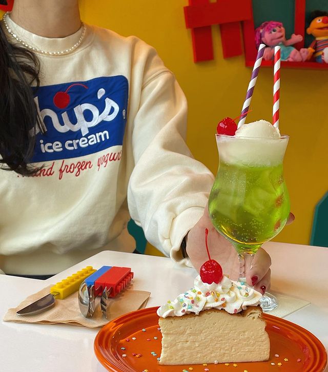 woman wearing a sweatshirt holding a drink with a cake on the table