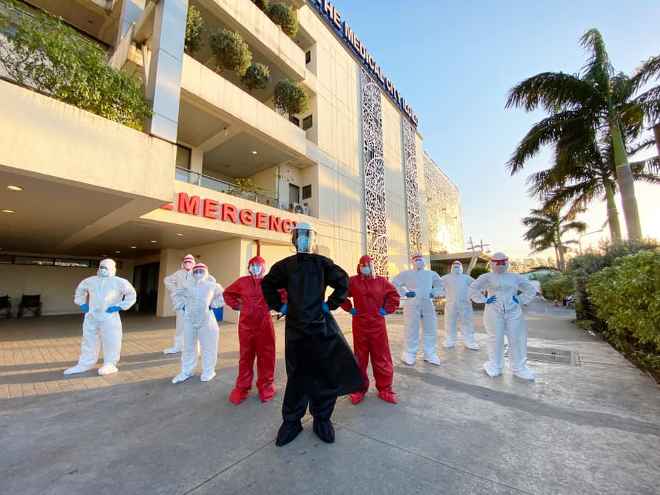 health workers wearing black, red, and white hazmat suits, in a triangle formation