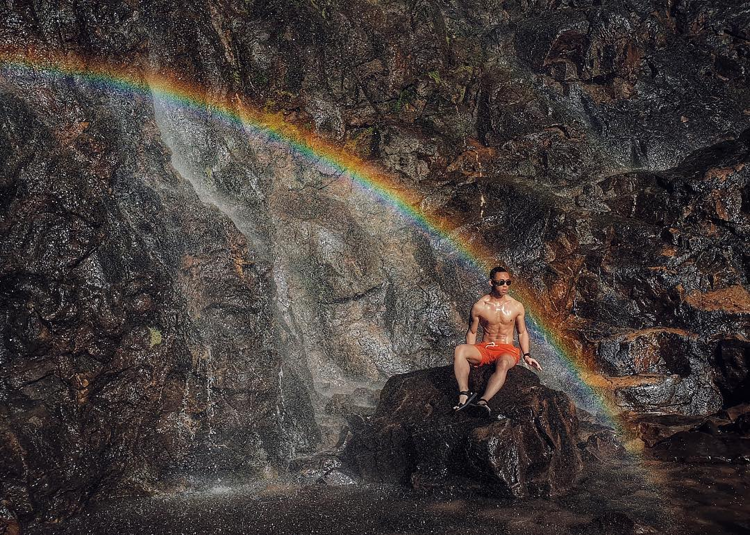 Guy posing under rainbow at Rainbow Waterfall